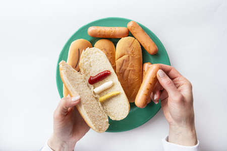 Fresh hot dog buns  on a green plate along with sausages. The girl holds in her hands a bun with sauces  which she puts a sausageの写真素材