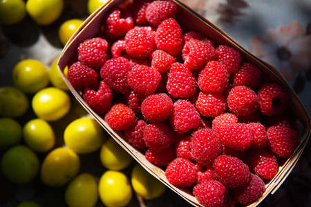 Fresh sweet juicy raspberries in a wooden basket close-up on a yellow cherry plum background. Close-up, beautiful sunset lightの写真素材