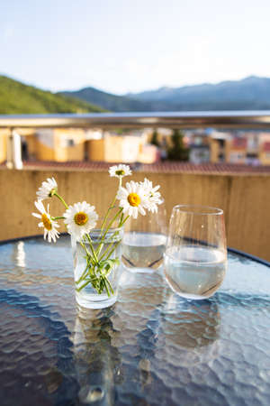 A bouquet of daisies in a glass vase with water stands on a glass table along with a glass of waterの写真素材
