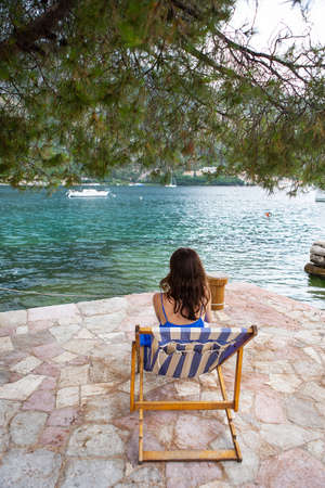 Very beautiful embankment of the Bay of Kotor, Montenegro. The girl sits on a striped chaise longue. The concept of rest and vacation in Europeの写真素材