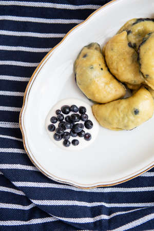 Sweet fruit dumplings with fresh forest blueberries. Homemade fresh dumplings on a plate along with sour creamの写真素材