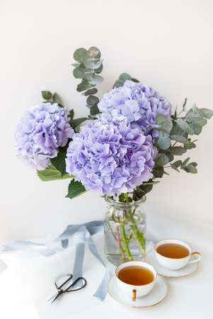 Two cups of black tea in a porcelain beautiful white cup with a gold cut. Beautiful bouquet of purple hydrangea on the table. Tea ceremony conceptの写真素材