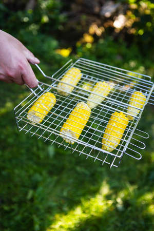 Delicious sweet corn is grilled on the grill. Outdoor recreation, close-up. Male hands are engaged in cookingの写真素材