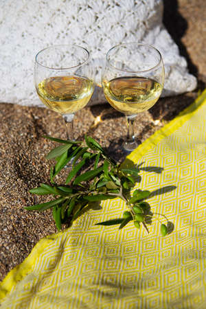 A picnic on a sandy beach with white wine, an olive branch, a wicker bag on a yellow blanket on a sandy beachの写真素材