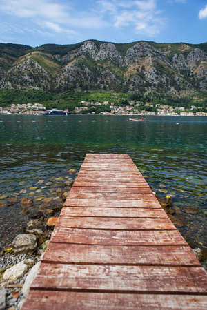 Long wooden pier against the backdrop of the beautiful Bay of Kotor, Montenegro. Very beautiful promenade and beach with clear blue waterの写真素材