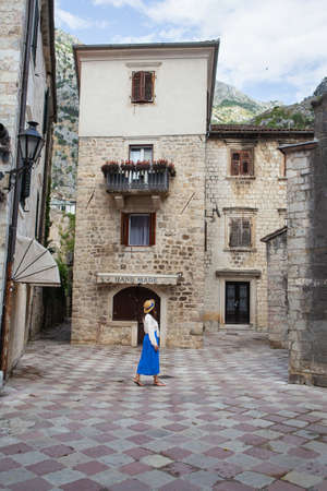 A girl in a blue dress and a straw hat walks through the old town of Kotor, Montenegroの写真素材