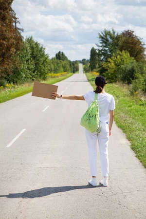 A beautiful girl with a backpack on her shoulder stands on the road brakes the car, hitchhiking, adventure, tourism, aloneの写真素材