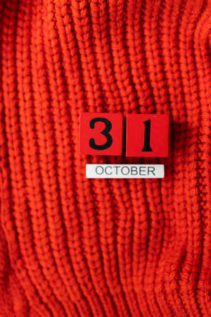 Wooden cube calendar showing October 31, Halloween isolated on red background red knitted sweaterの写真素材