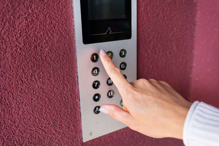 A young woman dials the apartment code on the panel of an electronic intercom. Protection and safety conceptの写真素材