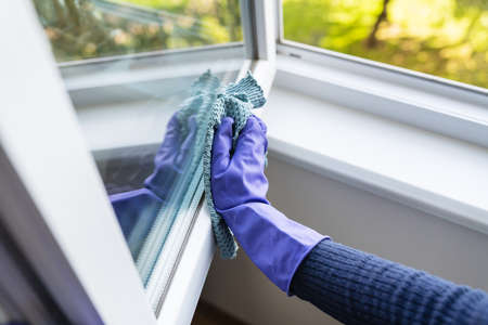 Cleaning and cleaning concept. A young girl in purple gloves wipes the dust on the windowsill and...