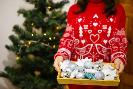 Female hands are holding a tray in which there are many beautiful multi-colored Christmas tree decorations. Christmas tree decoration process. New Year Christmas. 2022 year of the tigerの写真素材