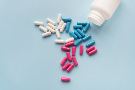 Various multicolored pills - blue, pink, white flying from an open plastic bottle, isolated on a light blue backgroundの写真素材