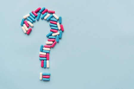 A question mark which consists of three different colorful vitamins on a blue background. Health issue and treatmentの写真素材