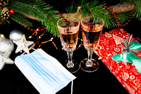 Christmas background with fir branches, two champagne glasses, gift, medical mask, concept of New Year's decor, close-upの写真素材