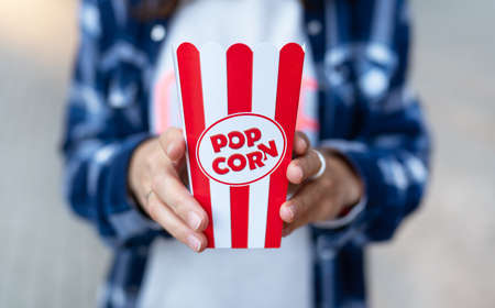 The girl holds in her hands a classic red box of popcorn outdoors. Going to the cinemaの写真素材