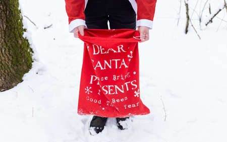 A man dressed as Santa Claus is holding a large red bag with gifts for childrenの写真素材