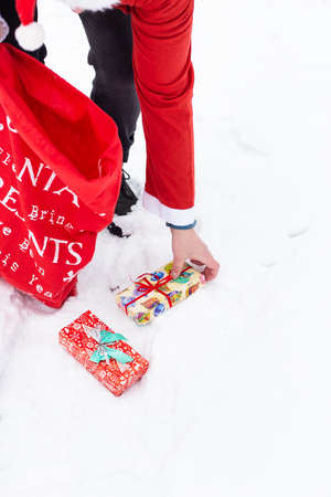 A man dressed as Santa Claus collects gifts in a snowy forest in the snow, colorful boxes with giftsの写真素材