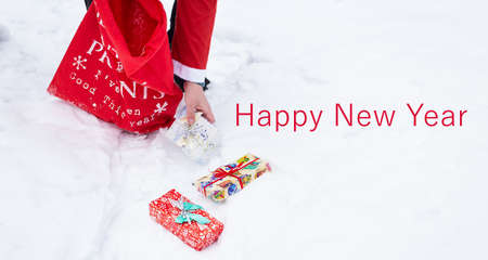 A man dressed as Santa Claus collects gifts in a snowy forest in the snow, colorful boxes with gifts. Happy New Year letteringの写真素材