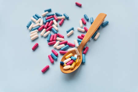 Various pills on a blue background together with a wooden spoon in which vitaminsの写真素材