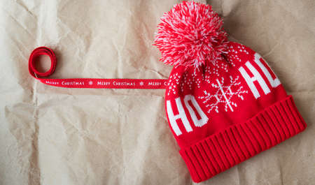 Red ribbon with the inscription Merry Christmas together with a red cap spread out on craft paper. Christmas concept on December 25thの写真素材