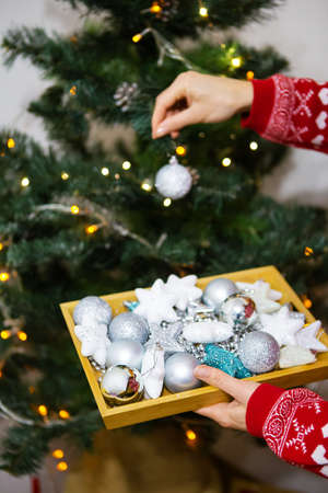 Happy girl holds a tray with Christmas toys in her hands and decorates the Christmas tree at home for Christmas, 2022 year of the tigerの写真素材