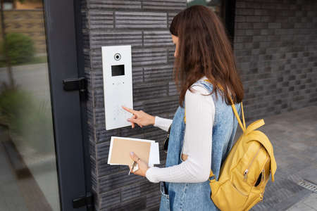 Door access control - a young woman student, holding a mail in her hands, enters the code to open the door. door codeの写真素材