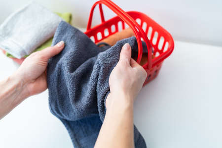 Multi-colored towels lie in a red laundry basket, a woman folds a towel. Laundry and ironingの写真素材