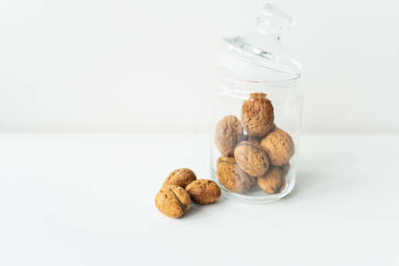 Beautiful whole walnut kernels in a glass jar, whole nuts in the shell can be seen nearby, on a...
