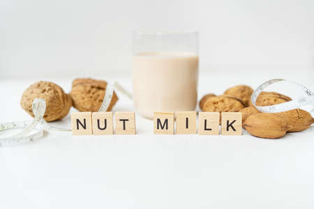 Vegan milk from nuts in a glass cup with various nuts on a white table. lettering nut milkの写真素材