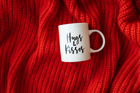 Hugs and kisses inscription on a white cup on a red knitted fabric. love concept. St. Valentine's Dayの写真素材