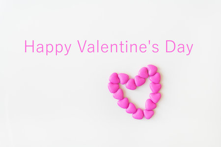 Valentine's day pattern background flat lay top view of heart shaped pink candies scattered on white background. Inscription happy valentine's dayの写真素材