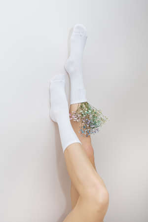 The legs of a girl in white socks in which there are flowers stand up. The concept of smooth and beautiful legsの写真素材