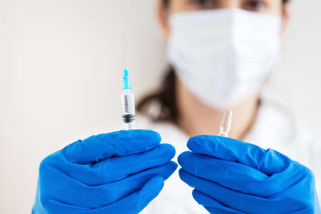 A young doctor with a syringe and a vaccine in his hands. Doctor indoors makes vaccination. A woman in a medical office. Vaccination against influenza and virusesの写真素材