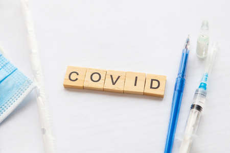The inscription covid on a medical background, next to the vaccine, syringe, pen, protective mask. medical theme. Concept: vaccination against coronavirusの写真素材
