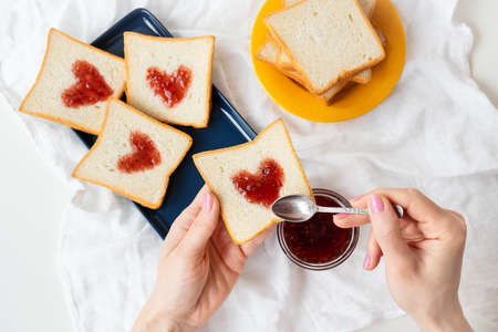 The girl makes a toast on which the heart is made of jam. Surprise breakfast concept in bed. Romance for St. Valentine's Dayの写真素材