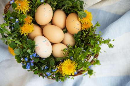 Beautiful spring bouquet in a wooden basket with Easter painted eggs, eggs with cute faces. Easter postcardの写真素材