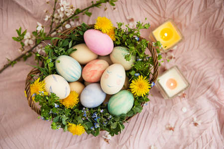 On a pastel bedspread is a basket of grass and bright flowers. The basket contains Easter eggs painted with watercolors in beautiful pastel colorsの写真素材