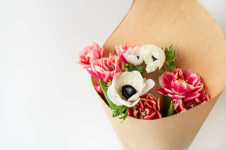 Beautiful red and white bouquet of tulips and anemones in kraft paper. The concept of spring and...