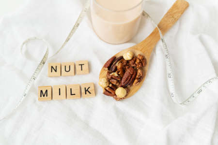 Vegan milk from nuts in a glass cup with various nuts on a white table, nuts in a wooden spoon. lettering nut milkの写真素材
