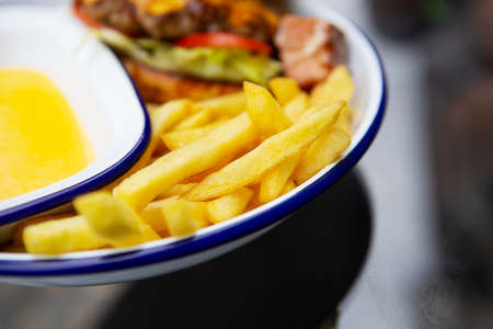 The concept of fast food. French fries lie on a meta plate along with cheddar cheese sauce and a...