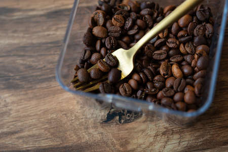 Roasted coffee bean in a plastic box along with a fork, close-up, top view. The concept of making coffeeの写真素材