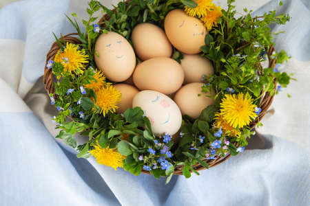 Beautiful spring bouquet in a wooden basket with Easter painted eggs, eggs with cute facesの写真素材