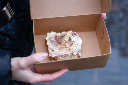 A girl holds a cinnabon with cream in a craft box. Fresh baked goods deliveryの写真素材