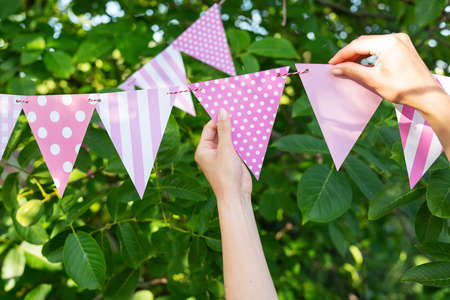 Triangular flags of a beautiful pink color, against the backdrop of a green garden. Festive decor - the concept of celebrating a birthday, anniversary, holidayの写真素材
