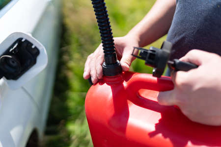The driver refuels the empty tank of the car from a red canister on the side of the road. Fuel...
