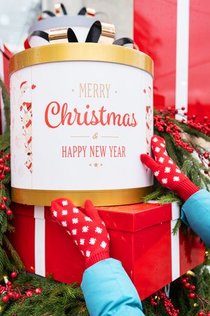 A girl on the street in red gloves holds a big red box in her hands. Christmas and New Year. Vertical photoの写真素材