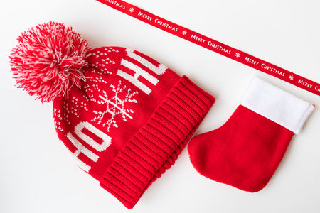Red ribbon with inscription Merry Christmas along with red hat, mittens, red sock laid out on white table. The concept of celebrating the New Year and Christmas on December 25の写真素材