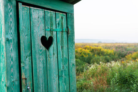 Heart shape on the old wooden toilet door, green toilet in the field. outdoor recreation. close-upの写真素材