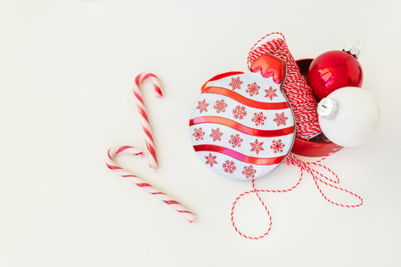 Christmas candies, along with toys for the Christmas tree and a red thread for wrapping gifts, lie on a white table. Selective focus, noise. Christmas and New Year 2023-2024. Place for an inscriptionの写真素材