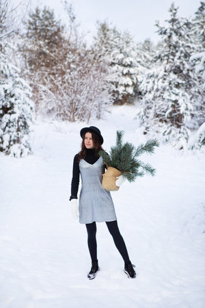 A young girl in a silvery dress and hat stands with her back in the middle of a beautiful winter forestの写真素材
